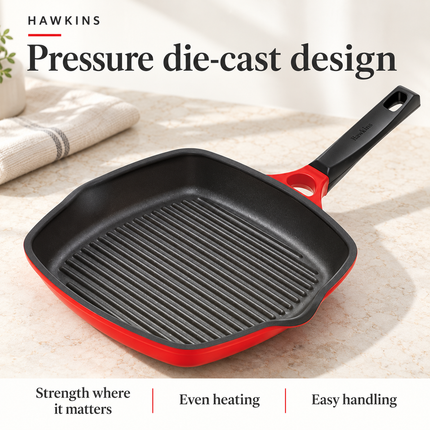 A Hawkins grill pan die cast 30cm with a red exterior and handle, shown on a light stone surface with promotional text reading 'Pressure die-cast design' and 'Hawkins'.
